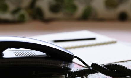 Telephone with notepad and pen on a table | Featured Image for the What to Include in Your On-Hold Phone Message Scripts for Maximum Impact blog.
